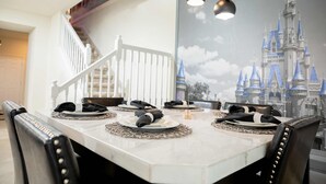 A dining area with a white table set for four, a mural of a castle, and a staircase in the background.