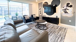 A modern living room with a large sofa, a coffee table, and a TV mounted on the wall.