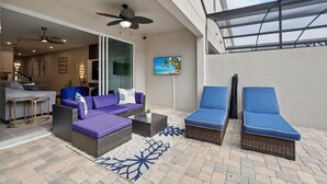 Une terrasse ensoleillée, dotée de meubles en osier, d’un téléviseur à écran plat et d’un ventilateur de plafond.