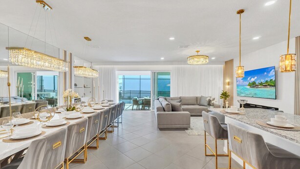 A modern dining area with a long table set for a meal, a sofa, and a TV in the background. - Last Minute Disney Getaway! Private Pool, Game Room & Themed Bedrooms. Book Now! #147905 (Orlando)