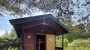 En liten stuga av trä med en veranda, en säng inuti och utsikt över den omgivande naturen.