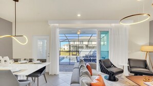 Ein modernes Wohnzimmer mit Essbereich, einer Couch, zwei schwarzen Sesseln, einem Tisch und Blick auf einen Pool und Gebäude im Freien.