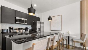 A modern kitchen with dark cabinetry, stainless steel appliances, and a central island with bar stools.