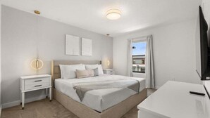 A modern bedroom with a large bed, bedside tables, a TV, and a view of the outside.