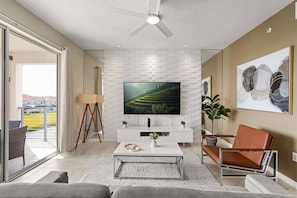 A modern living room with a flat-screen TV, white brick wall, and a balcony view.