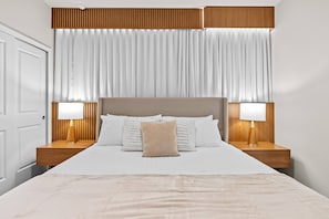Une chambre d’hôtel avec un grand lit, deux tables de chevet avec des lampes, une tête de lit en bois et une grande fenêtre avec des rideaux.