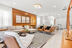 A modern living room with a sofa set, a dining area, and a kitchen in the background.