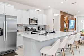 A modern kitchen with white cabinetry, stainless steel appliances, and a central island with bar stools.