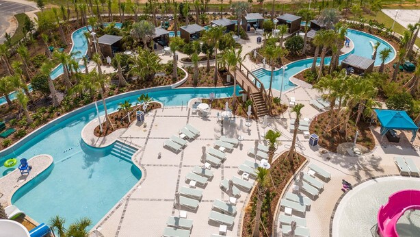 Un resort con un'ampia area piscina, diverse poltrone relax e uno scivolo d'acqua.