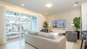 Un soggiorno moderno con un divano grigio, un tavolino da caffè e una TV fissata al muro. È presente una porta scorrevole in vetro che dà su una zona esterna con una panca e un tavolo.