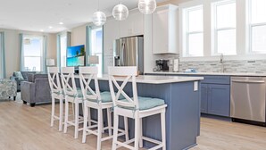 A modern kitchen with a central island, bar stools, stainless steel appliances, and a large window providing natural light. - Las Brisas (Port St. Joe)