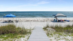 A beach with a wooden pathway leading to a sandy area with two beach umbrellas and a canopy. - Las Brisas (Port St. Joe)