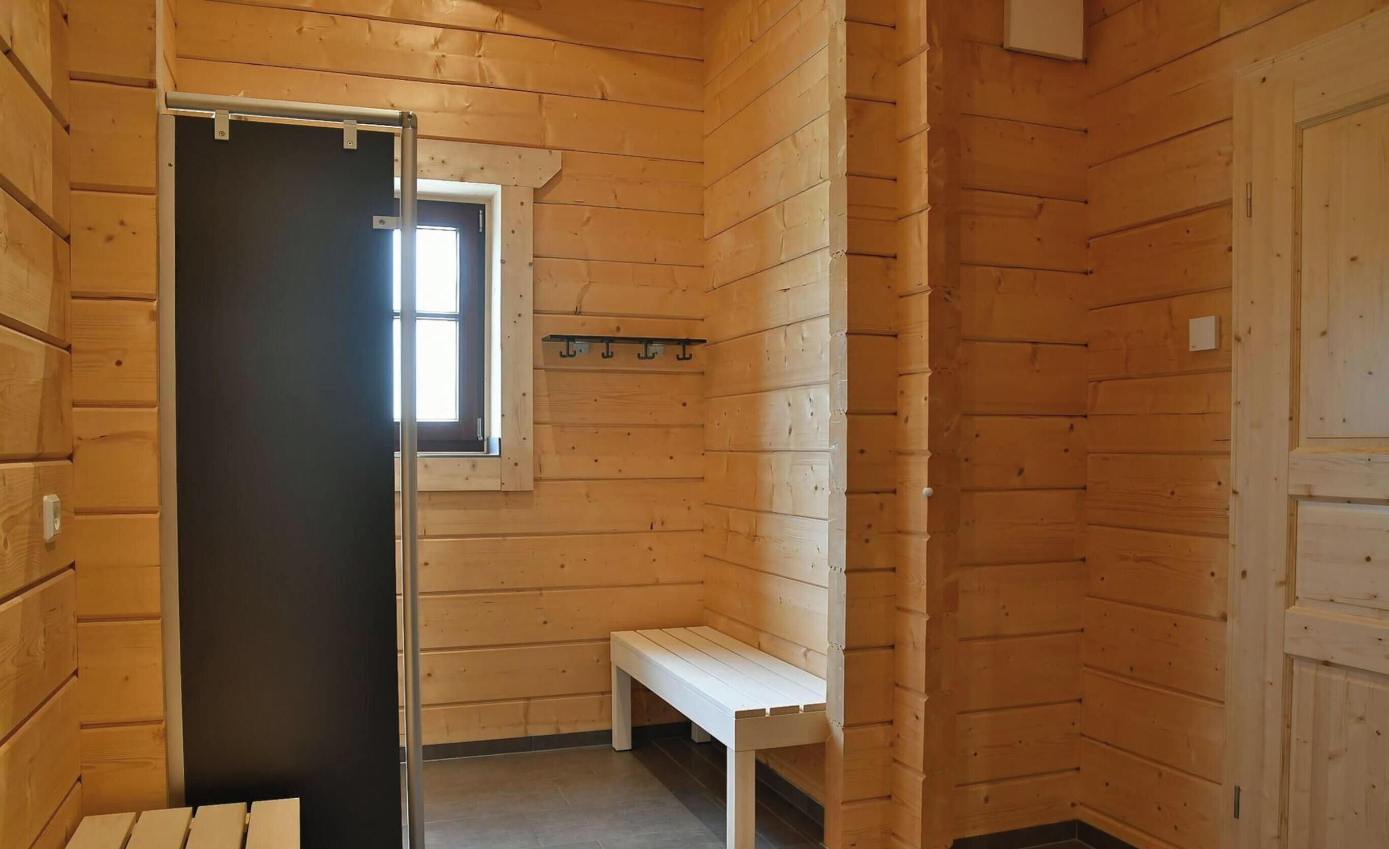 A wooden sauna room with a bench, a small table, and a window.