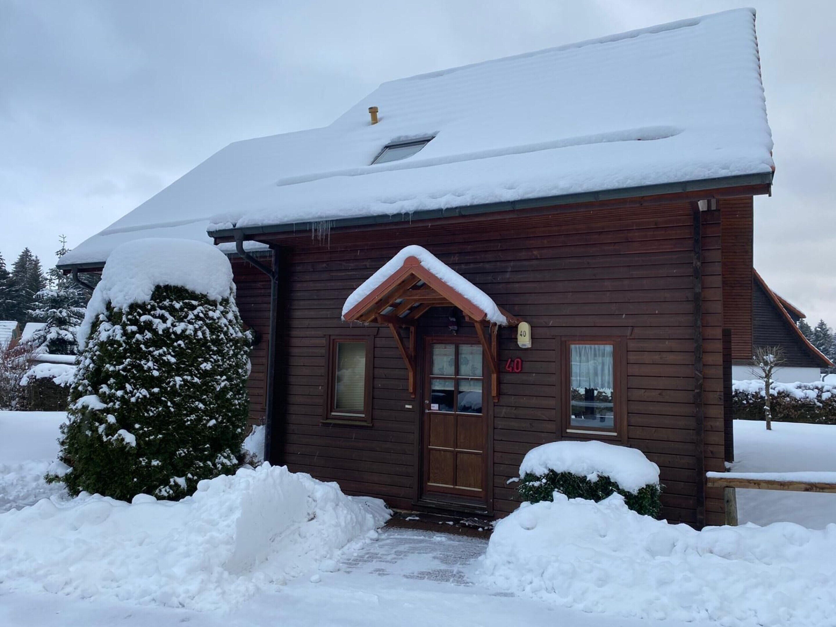 Una cabaña de madera con techo nevado y un pequeño porche.