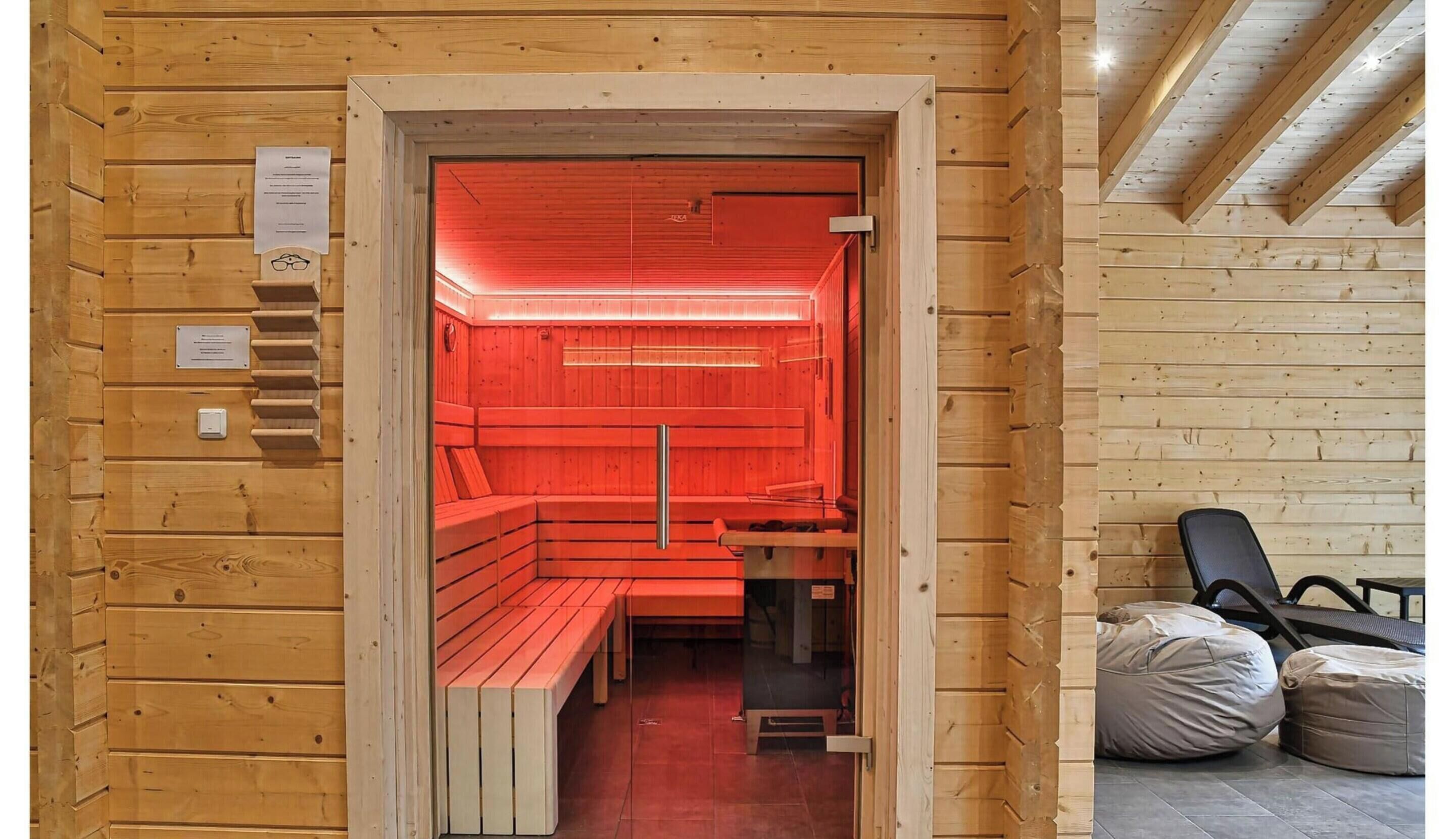 A sauna with wooden walls and benches, a glass door, and a ceiling with wooden beams.