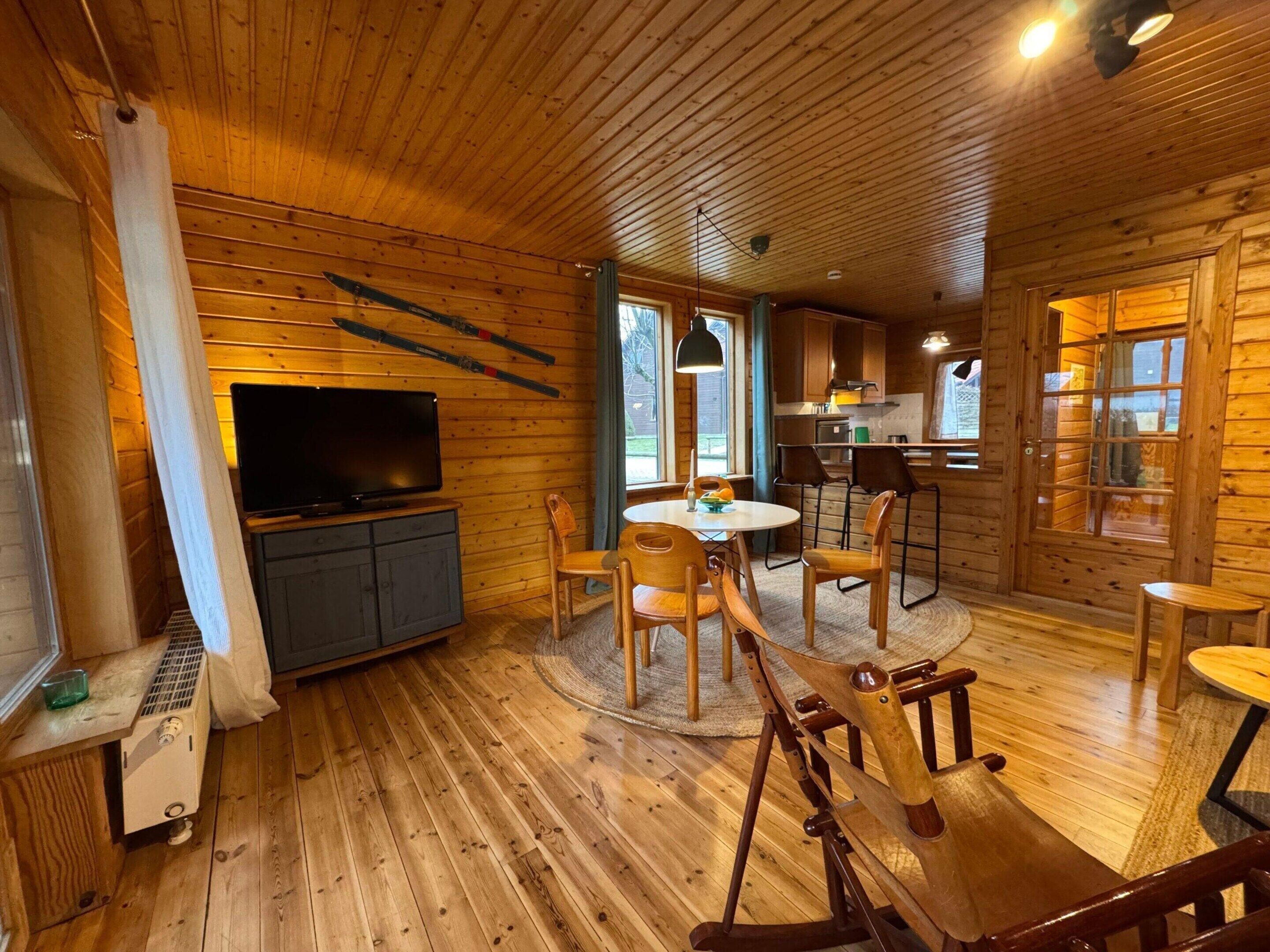 A wooden cabin interior with a TV, dining area, and kitchen.