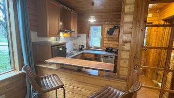 A wooden cabin with a kitchen area, two bar stools, and a window with curtains.