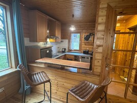 A wooden cabin with a kitchen area, two bar stools, and a window with curtains.