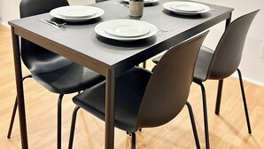 Un coin repas avec une table dressée pour quatre personnes, entourée de chaises, dans une cuisine moderne où l’on aperçoit des placards et un plan de travail à l’arrière-plan.