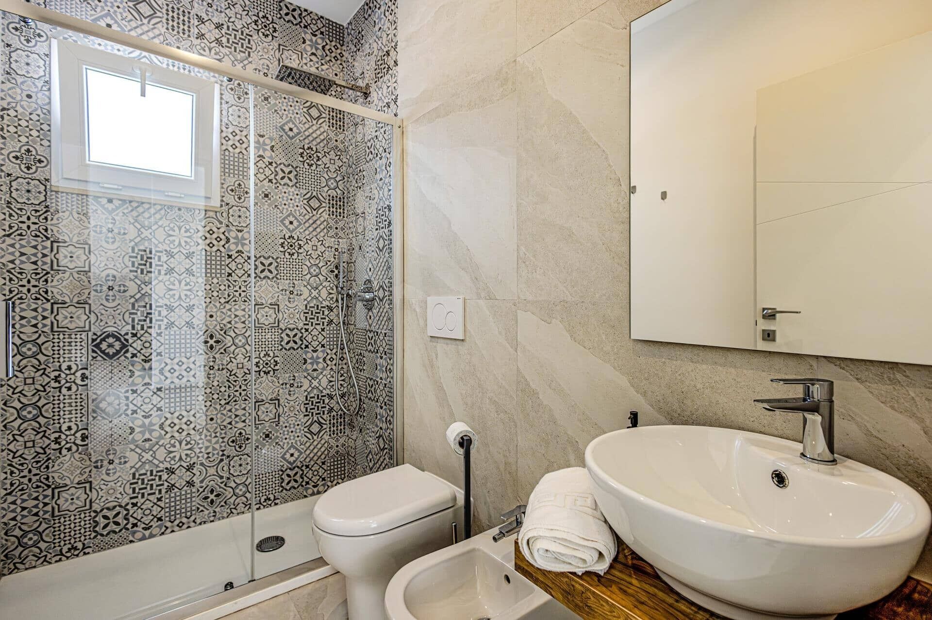 Une salle de bain avec des carreaux décorés, des toilettes, un bidet, un lavabo et un miroir.