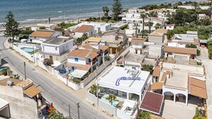 Vue aérienne d’un quartier résidentiel situé sur la côte, avec différents types de bâtiments, dont la villa Kennedy, qui possède une piscine et un panneau solaire.