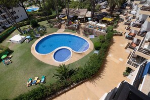 Una gran piscina rodeada de sillones de descanso y sombrillas, con un edificio al fondo.
