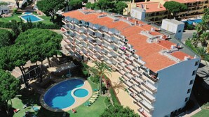 Un hotel a più piani con piscina sul tetto, un giardino curato e un’area parcheggio.