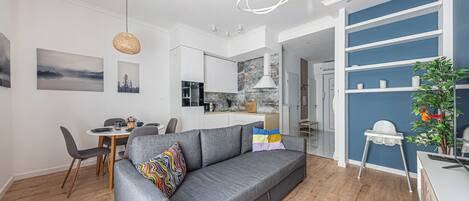 Un apartamento moderno con un sofá gris, una zona de comedor, una cocina y una pared de acento azul.