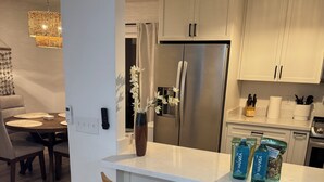 A modern kitchen with white cabinets, stainless steel appliances, and wooden bar stools. - Traveling Nurse Haven - 3BR, Furnished, WiFi, AC (Hilo)
