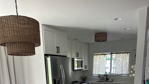 A modern kitchen with white cabinets, stainless steel appliances, and a dining area with a wooden table and grey chairs. - Traveling Nurse Haven - 3BR, Furnished, WiFi, AC (Hilo)