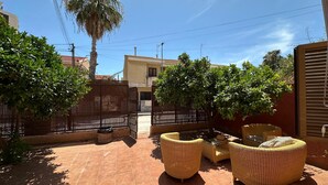 Un patio con muebles de mimbre, piso de baldosas y vistas a edificios vecinos.