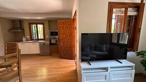 Un espacio habitable compacto con kitchenette, una mesa de comedor de madera, un sofá y un mueble para televisión.