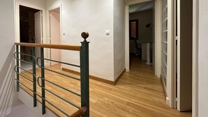 Una escalera con barandilla de madera y balaustradas de metal, que conduce a una habitación con piso de madera y paredes blancas.