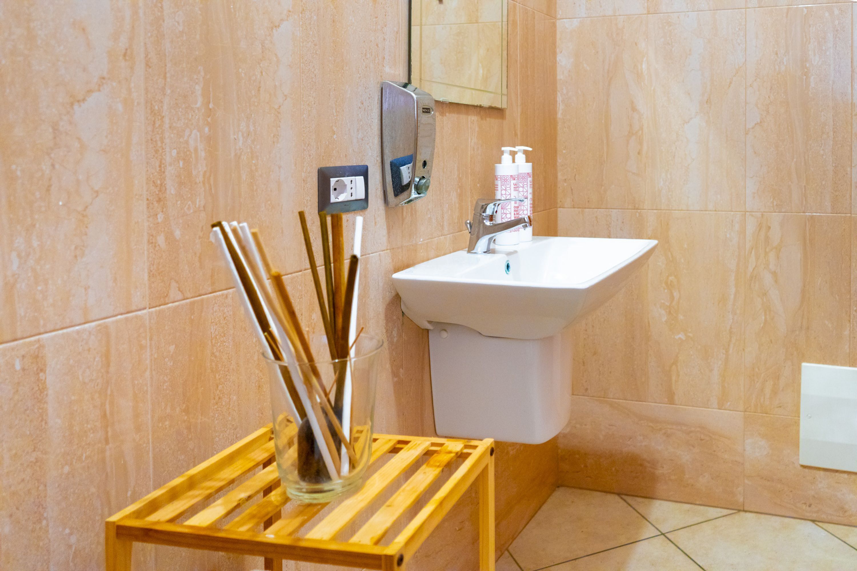 A bathroom with a sink, mirror, and a wooden shelf holding a glass vase with reeds.