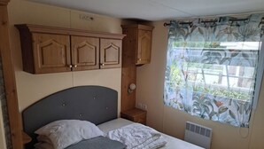 A bedroom with a bed, wooden cabinets, a window with a curtain, and a wall-mounted heater.