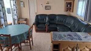 A living room with a black leather sofa, a wooden dining table with a green tablecloth, and a wooden cabinet with a decorative top.