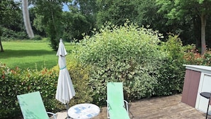 A wooden deck with two green lounge chairs and a round table with a white umbrella.