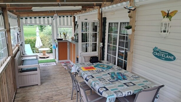 A covered patio area with a table and benches, a small garden visible through the open door, and a sign on the wall reading "CASTELANE".