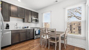 Una cocina moderna con armarios oscuros, un microondas de acero inoxidable y un comedor con mesa y sillas.