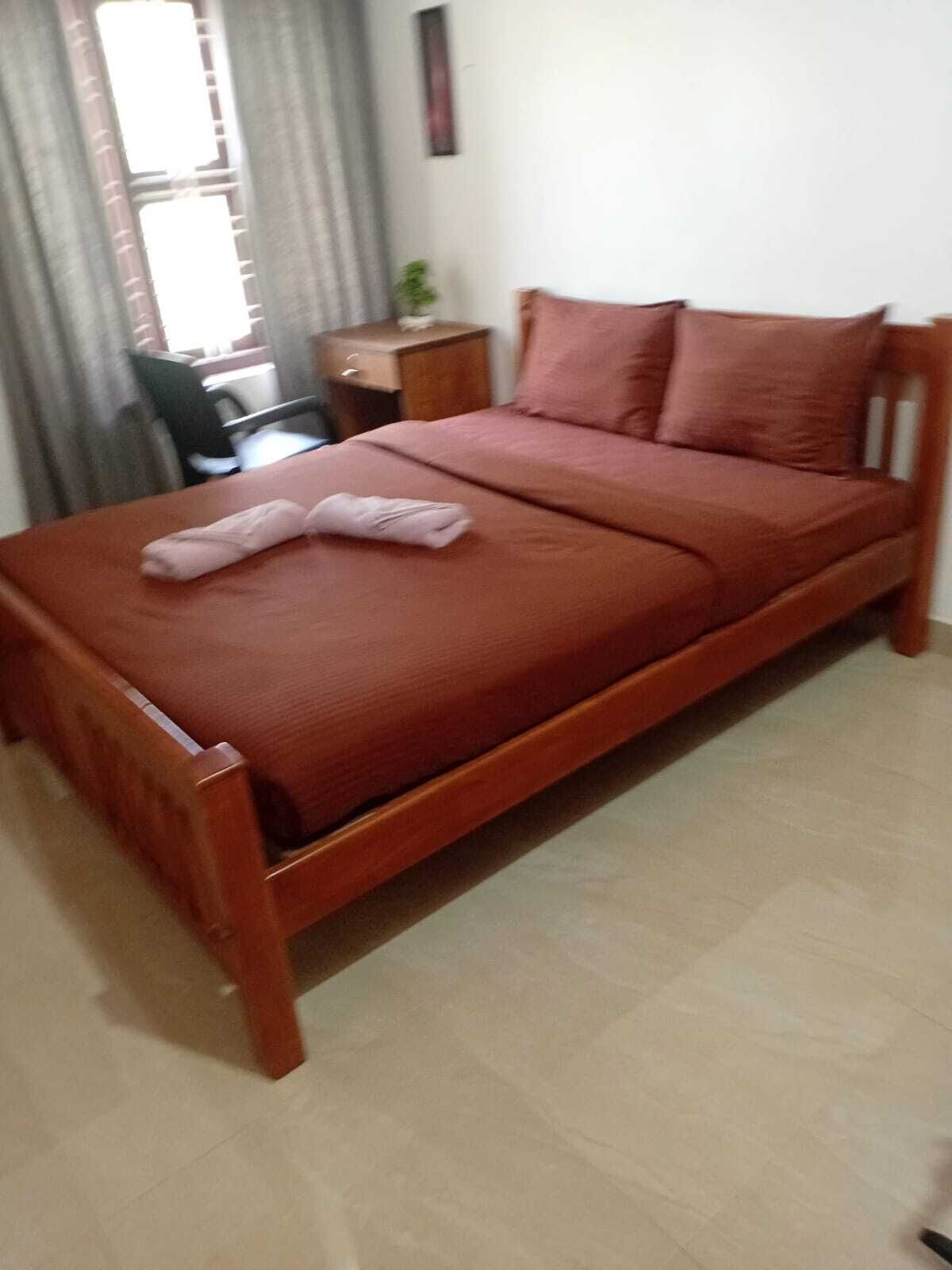 Un lit simple avec un cadre en bois et une couverture rouge, accompagné de deux oreillers.