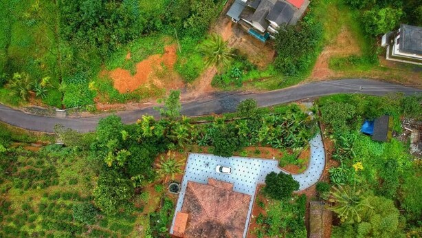 Vista aérea de uma propriedade com grande área aberta, entrada pavimentada e um edifício com formato de telhado característico.