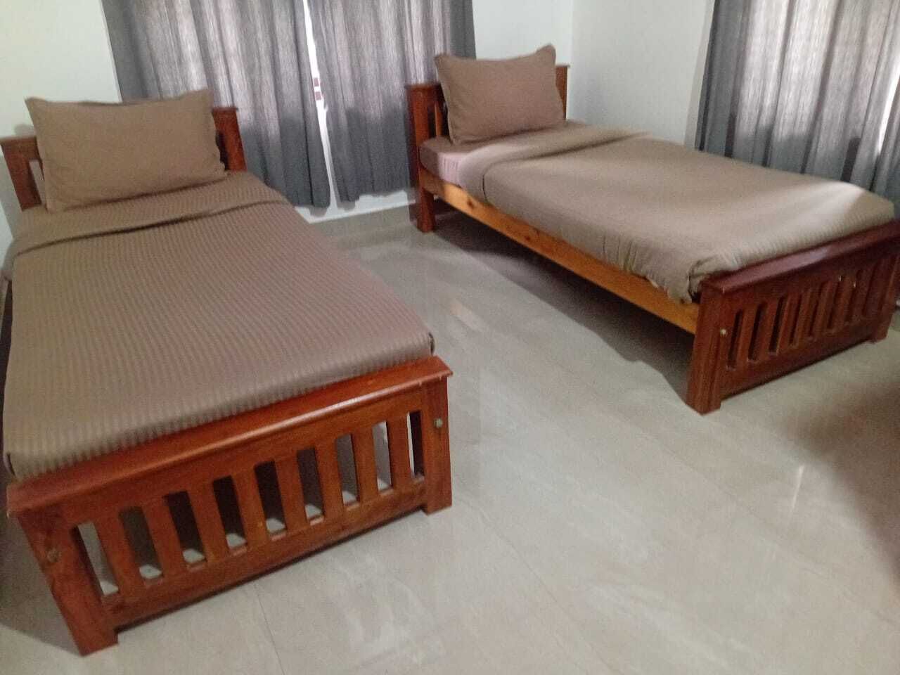 Two wooden beds with headboards and footboards, a grey curtain, and a light-colored floor.
