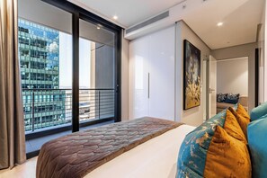 A modern bedroom with a large bed, a view of a cityscape through a sliding door, and a balcony with a railing. - Stunning Apartment with City Views (Cape Town)