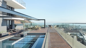 Un área de piscina moderna en la azotea con barandas de cristal, terraza de madera y sillones de descanso.