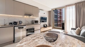 A modern kitchen with built-in appliances, a dining area with a stone table, and a balcony with a view of a building. - Stunning Green Point Apartment (Cape Town)