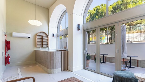 A modern hotel lobby with a reception desk, seating area, and large glass doors leading to an outdoor space. - Stunning Green Point Apartment (Cape Town)