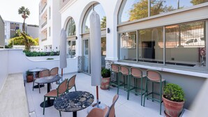 An outdoor patio with round tables and chairs, a large window with a view of the street, and potted plants. - Stunning Green Point Apartment (Cape Town)