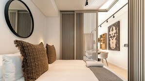 A modern bedroom with a large bed, a round mirror, and a view of a dining area through a sliding door. - Stunning Green Point Apartment (Cape Town)