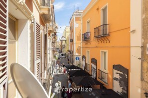 A narrow street with buildings on either side, some with balconies and outdoor seating areas.