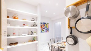 A modern kitchen with white cabinetry, a dining area with a table and chairs, and a colorful abstract painting on the wall.